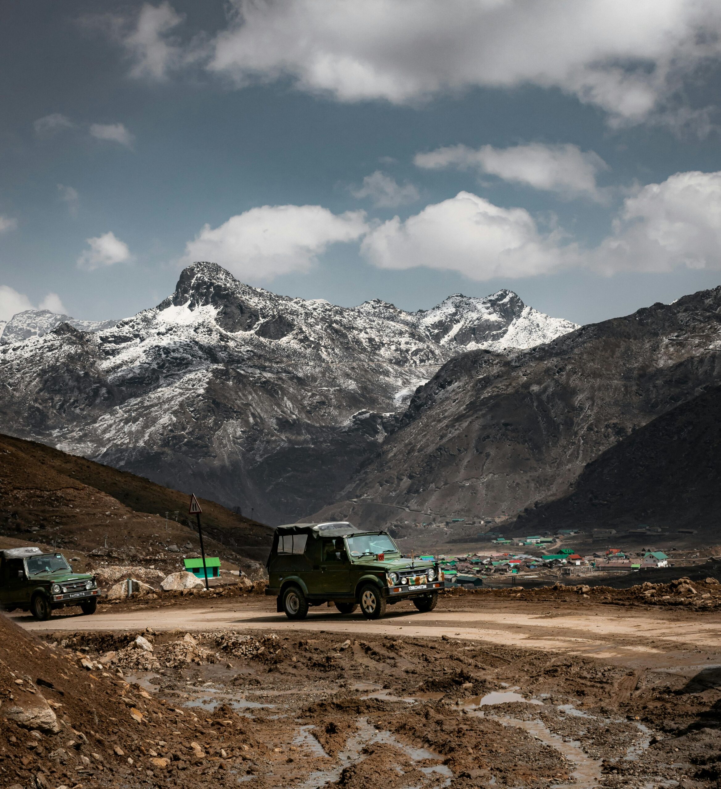 A rugged Jeep traversing an unpaved mountain road in the Himalayas with majestic snow-capped peaks in the background.