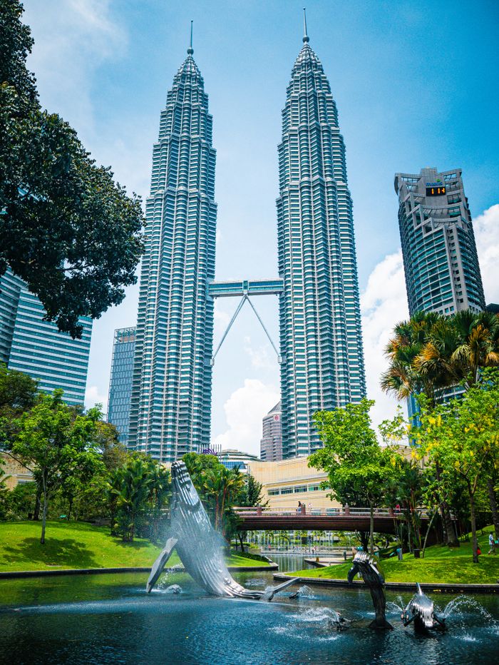 View of Petronas Twin Towers and surrounding park in Kuala Lumpur under a blue sky.